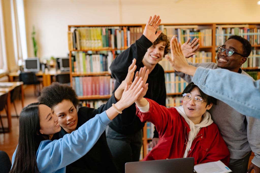 group of students high-fiving in a library because of the Million Dollar Community College Challenge.
