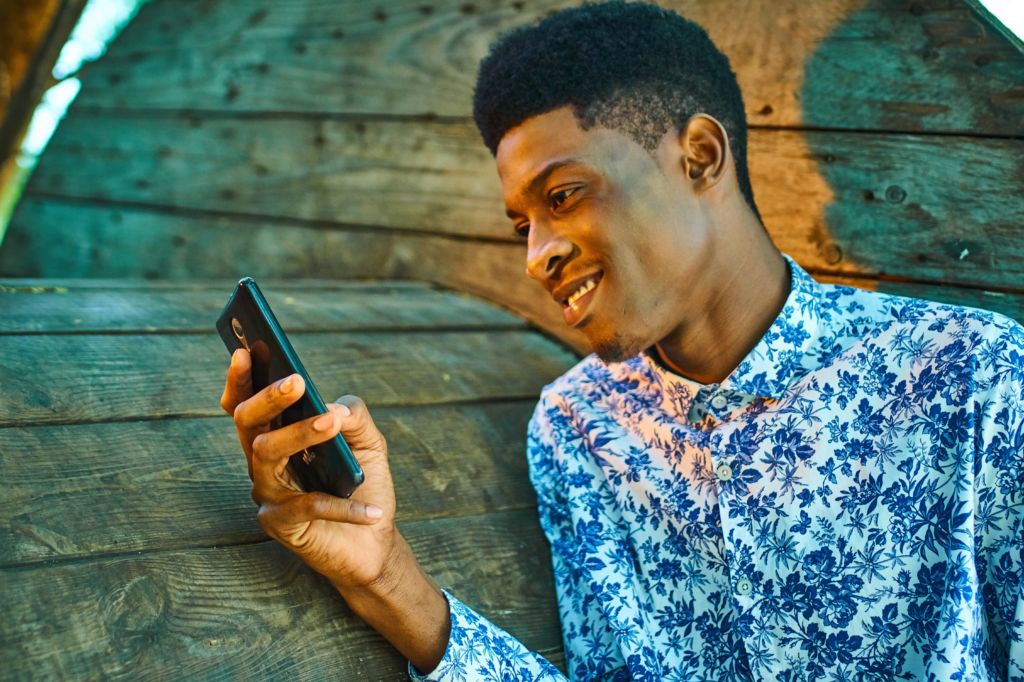 A young male student smiles at his phone... hopefully because you sent him an encouraging message to enroll!