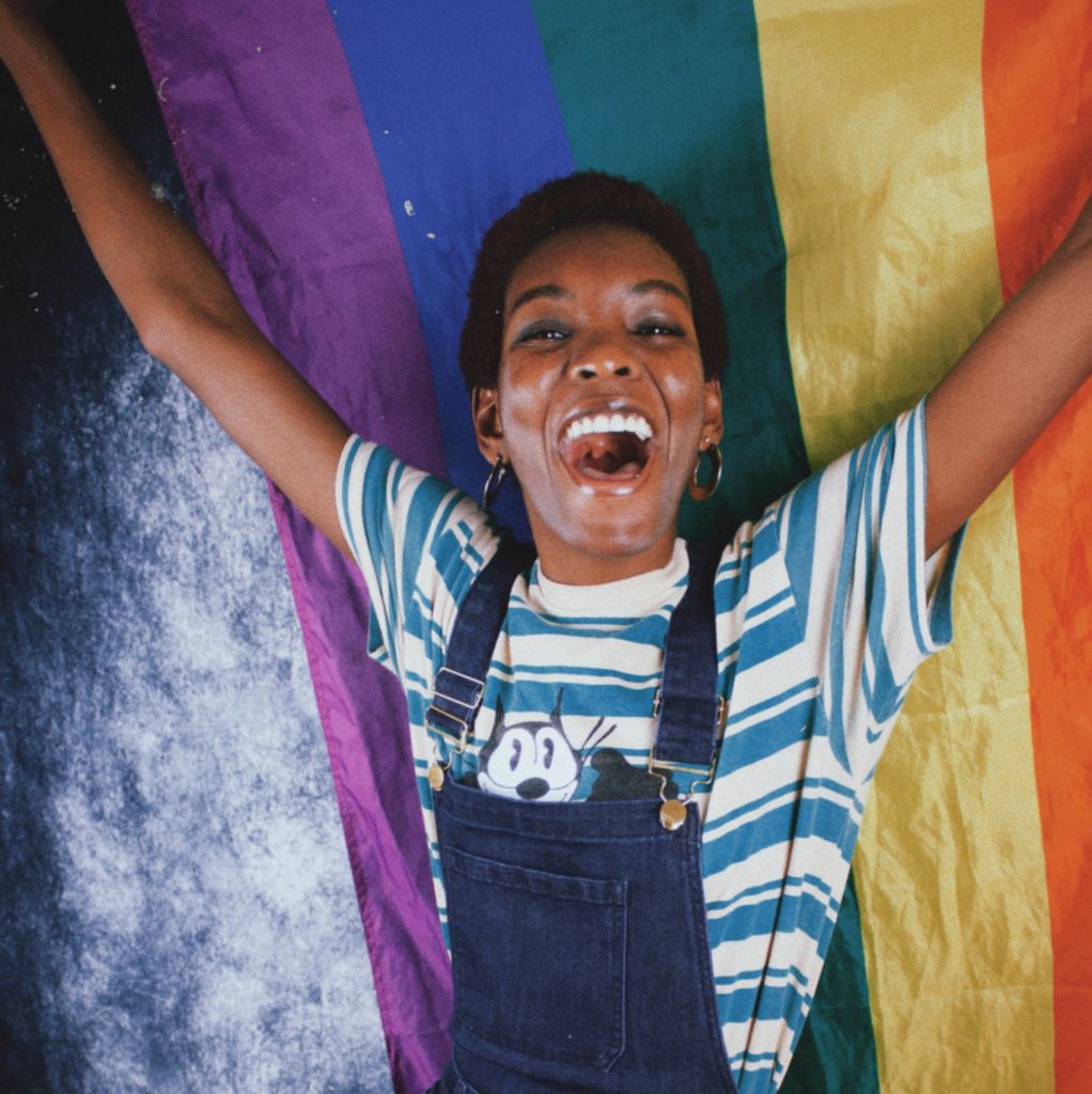 A young Black LGBTQ+ person holds up a rainbow flag for Pride Month 2022
