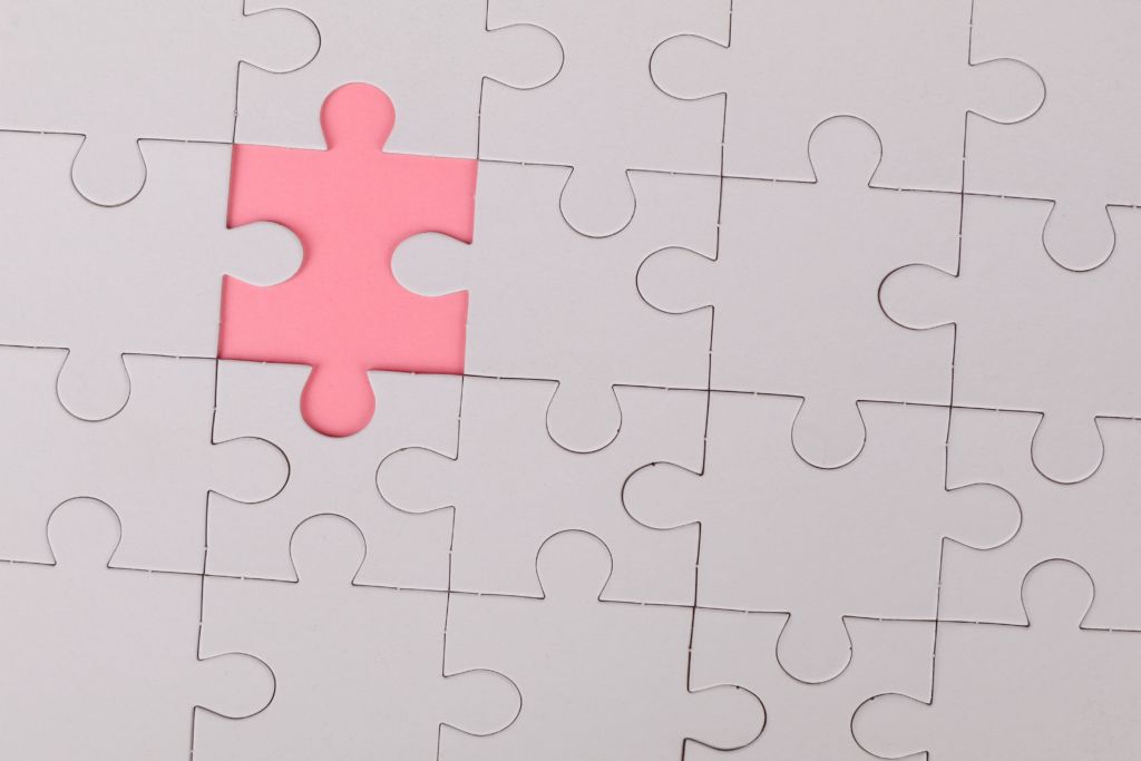 White puzzle with one missing piece highlighted pink. 