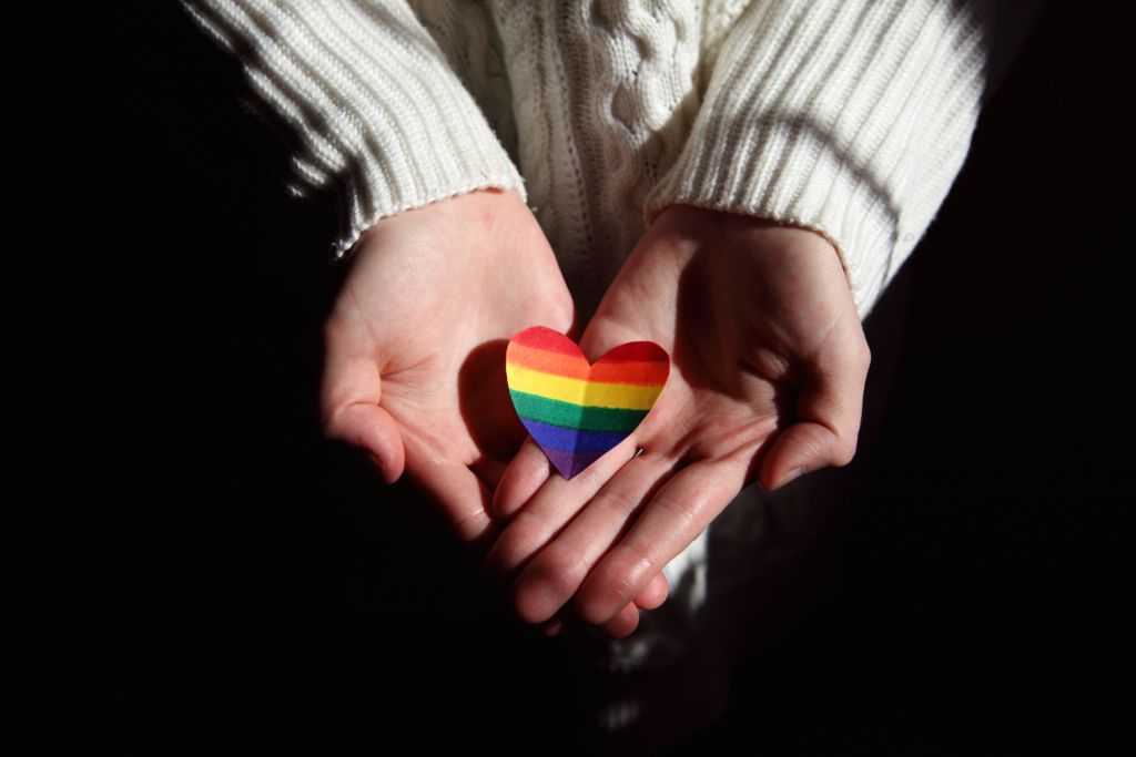 Hands cupped around a heart with an LGBTQ rainbow for Pride Month 2022