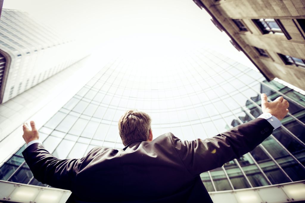 A young man throws his hands wide in front of a skyscraper, showing growing opportunity. To strengthen male student enrollment, show men the opportunities they can find at community college. 