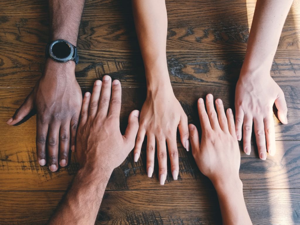 Four hands together on a table of different skin colors.