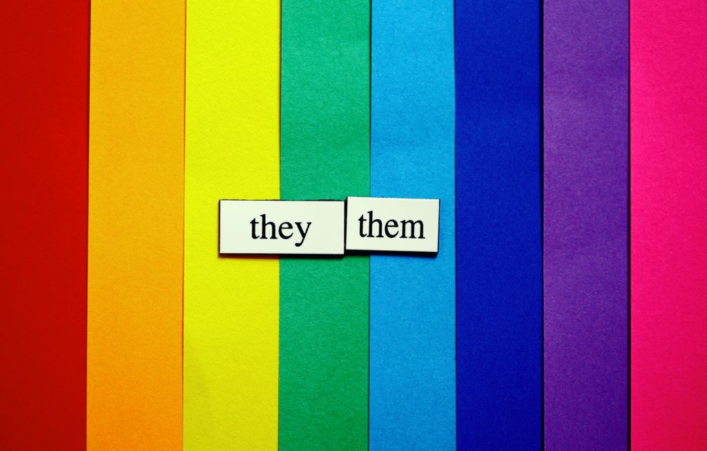 They/them written over a rainbow background. Elle pronouns in Spanish are equivalent to they/them pronouns in English and something to take note of this Hispanic Heritage Month.