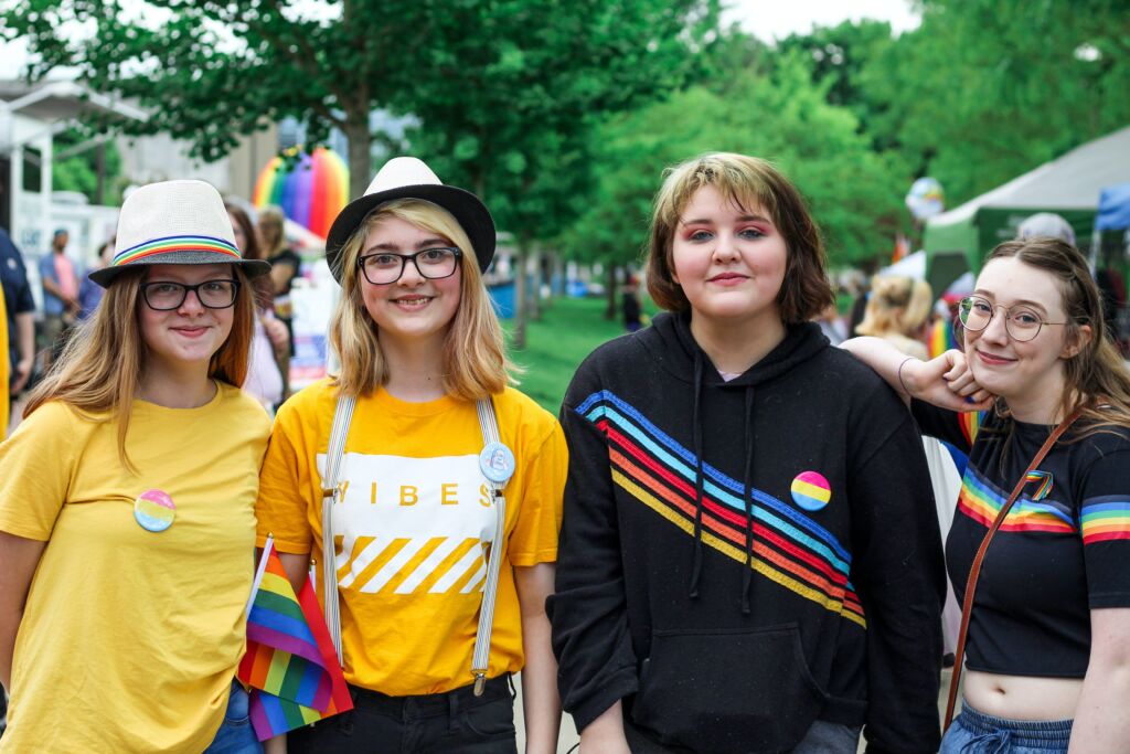Four friends decked out in rainbows attend LGBTQ Pride.