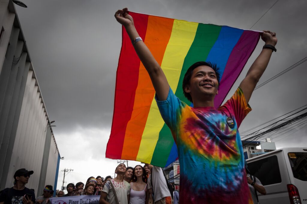 A young person holds up a rainbow flag.